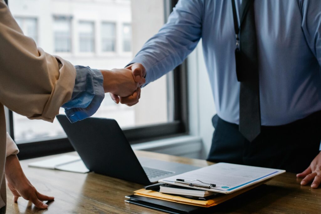 pexels-photo-5673488-5673488 Crop unrecognizable coworkers in formal wear standing at table with laptop and documents while greeting each other before meeting